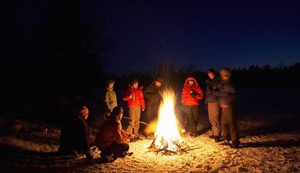 Eine Personengruppe steht nachts um ein Feuer.