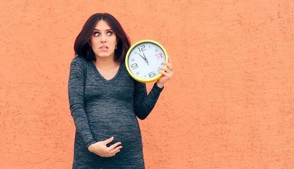Wann kommt das Baby? Schwangere Frau schaut besorgt auf eine grosse Uhr