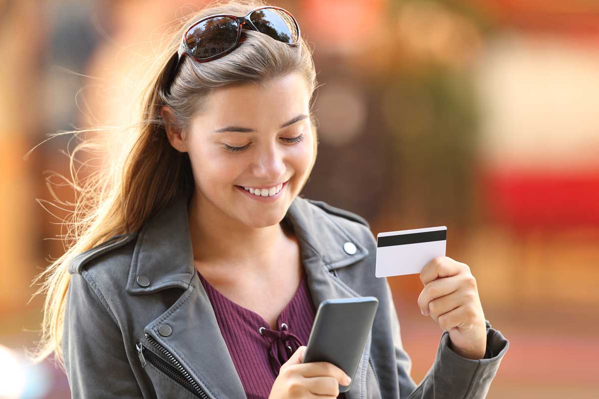 Eine junge Frau steht auf einer Strasse mit Smartphone und Kreditkarte.