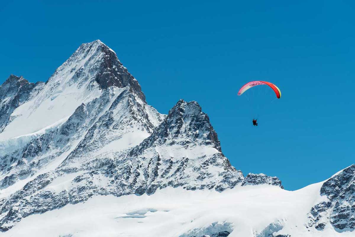 Gleitschirmflieger bei blauem Himmel in den Schweizer Bergen.