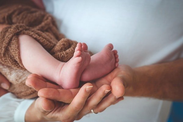 Hände von Eltern halten Neugeborenes