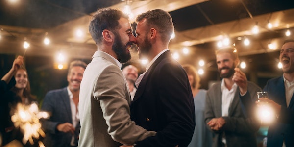 LGBT-Hochzeitspaar küsst sich vor feiernden Gästen.