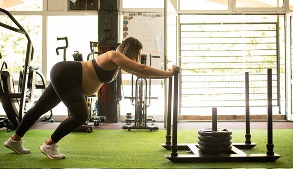 Sport in der Schwangerschaft: Schwangere Frau trainiert im Fitnessstudio mit Gewichten. 