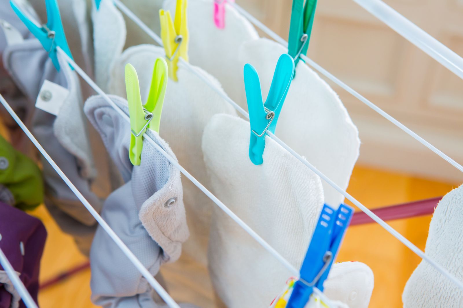 Einlagen von Stoffwindeln sind mit bunten Wäscheklammern an Wäscheständer geklemmt
