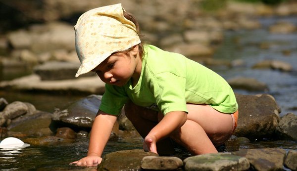 Flüsse Schweiz: Dieses Mädchen spielt an einem Fluss mit Steinen