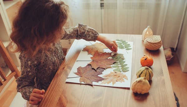 Herbstbasteln mit Kindern: Ein Mädchen macht eine Collange mit Blättern