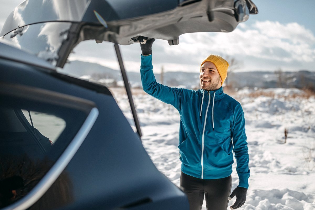 Ein Mann öffnet den Kofferraum seines Elektroautos im Winter