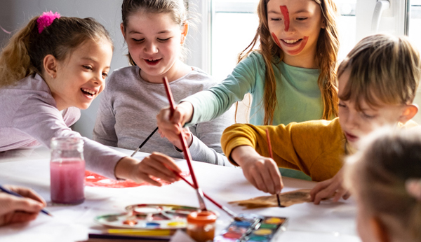 Vier Mädchen und ein Junge mit Pinseln und Farbkästen sind am malen und basteln, sie lachen und haben Spass.
