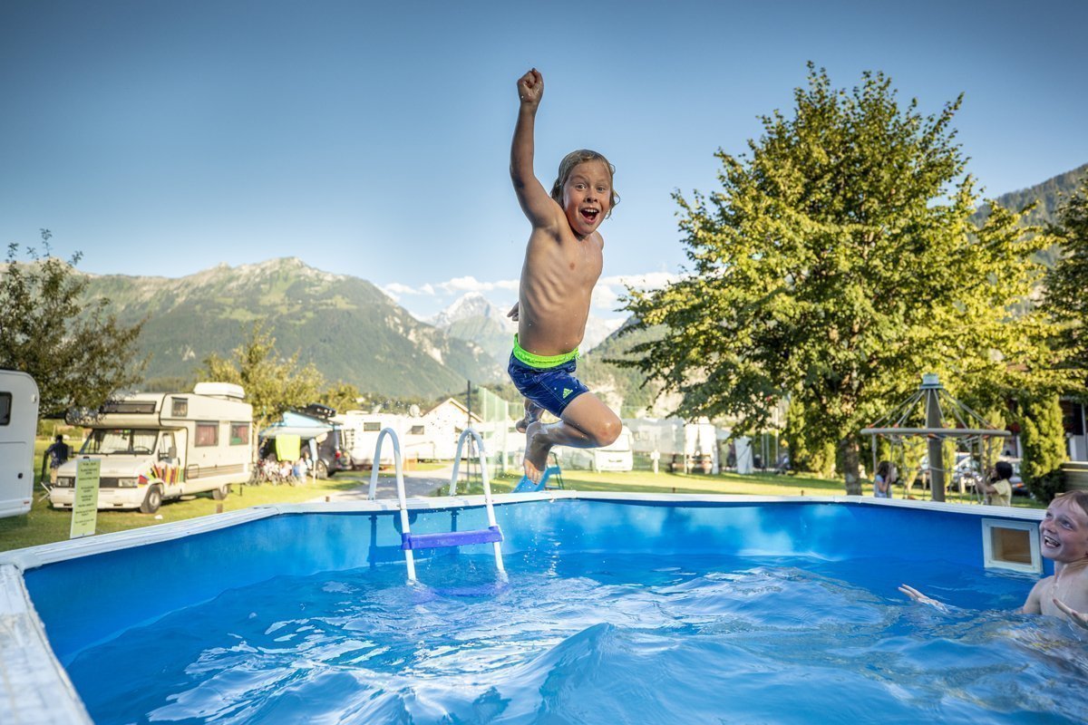 ein Kind springt in den Pool und schaut dabei lachend in die Kamera