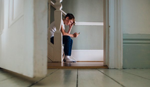 Junge sitzt traurig mit Smartphone auf Treppe Cybermobbing
