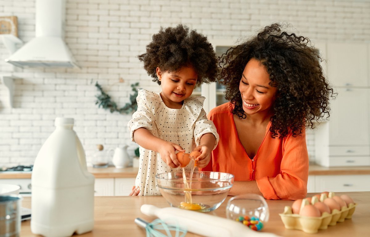 Eine Mutter kocht mit ihrem kleinen Kind und fördert damit die Feinmotorik ihrer Tochter.