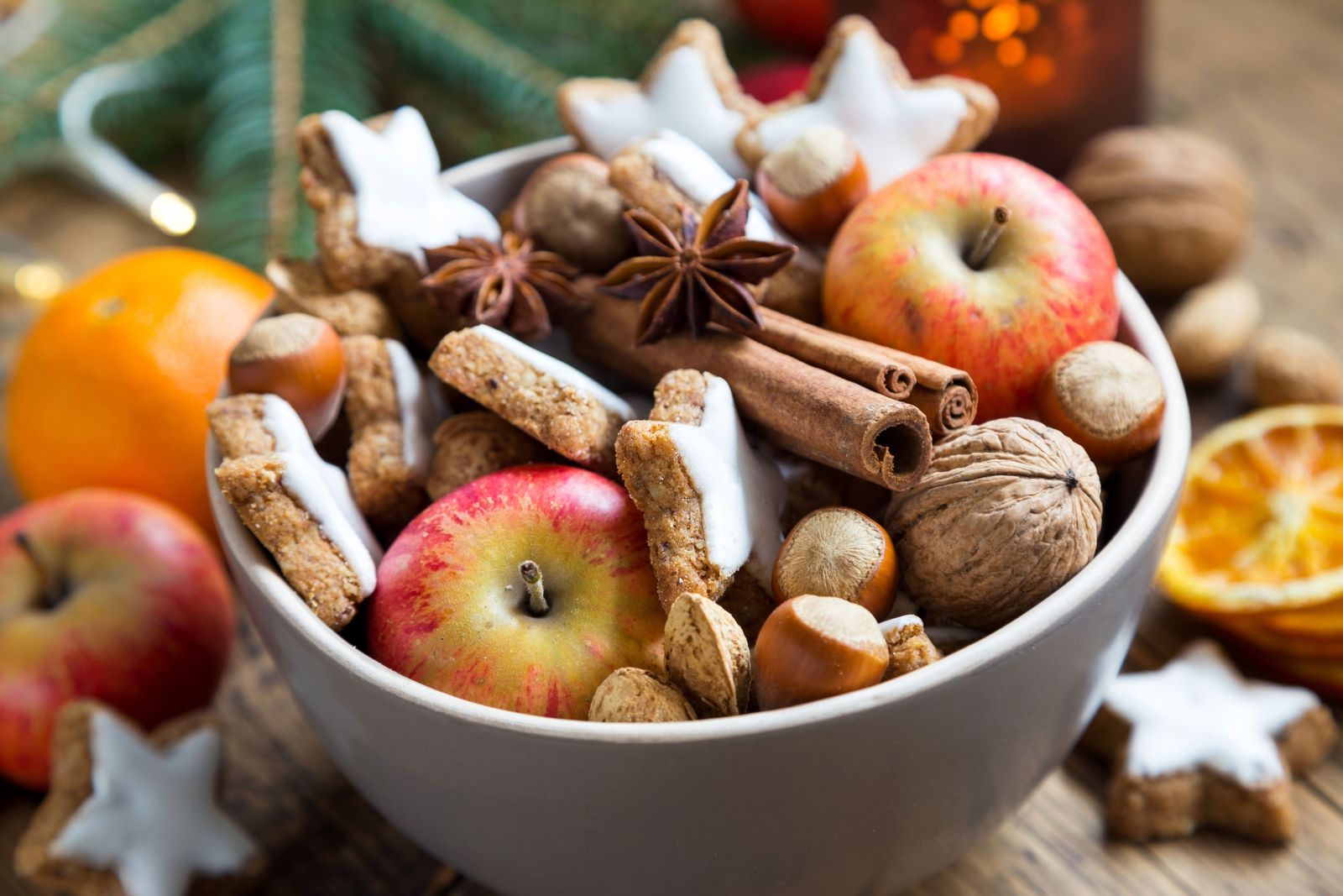 Ein Schale mit Zimtsternen, Äpfeln und anderen weihnachtlichen Dingen auf einem Holztisch.