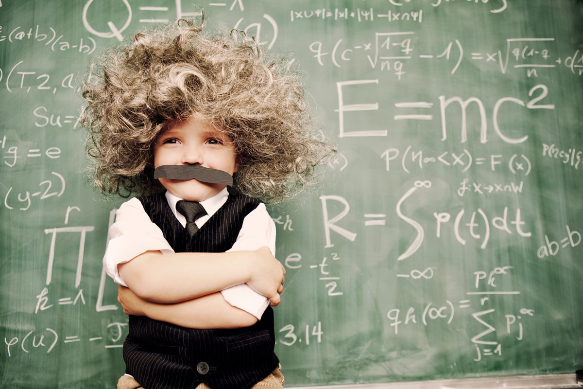 Ein Kind verkleidet als Einstein vor einer Wandtafel.