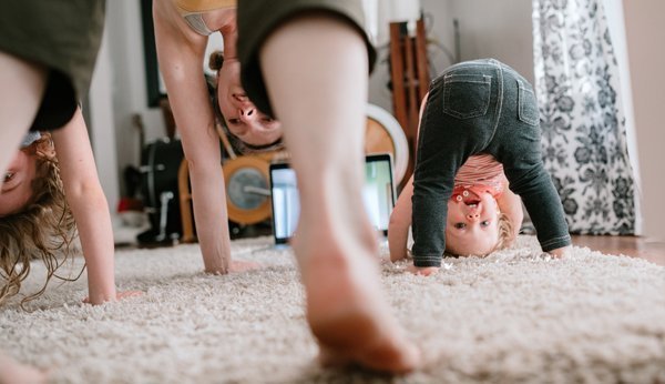 Bewegungsförderung: Mutter und zwei Kleinkinder machen Sport im Wohnzimmer