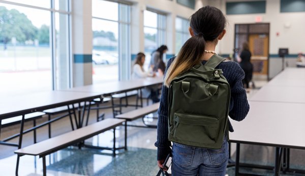Mobbing in der Schule: Mädchen steht alleine in Schulzimmer, Rückenansicht. 