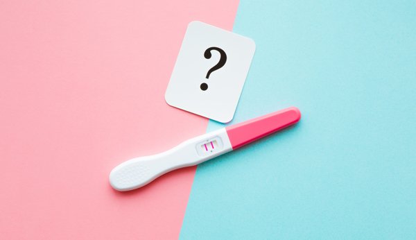 À quelle semaine de grossesse suis-je? Calcul de la semaine de grossesse: test de grossesse positif et point d'interrogation sur un fond coloré. 