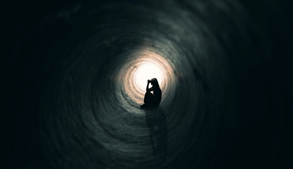 Spätfolgen Mobbing: Frau sitzt in einem dunklen, engen Tunnel