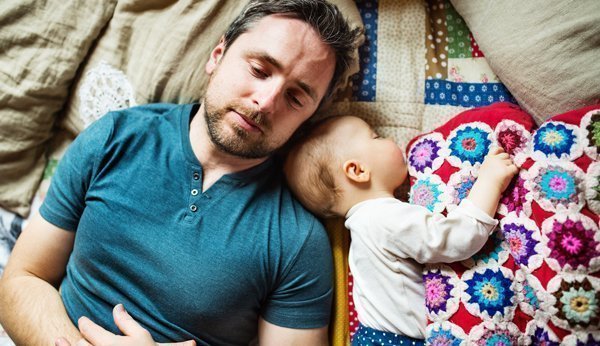 Wieviel Papizeit braucht es? Vater schläft neben Baby auf der Couch.