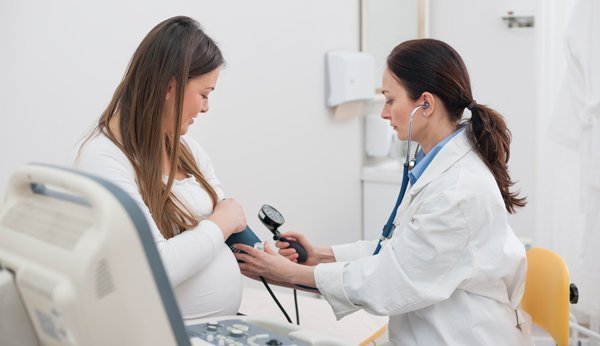 Schwangere Frau und Ärztin. Die Ärztin misst den Blutdruck der Patientin. 
