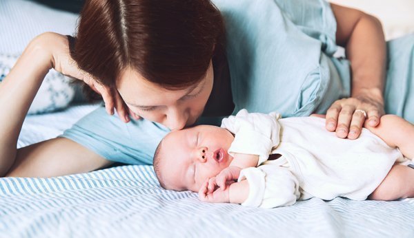 Wochenbett: Mutter gibt ihrem Neugeborenen ein Küsschen auf den Kopf. 
