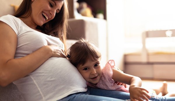 Schwangere Mutter mit kleiner Tochter: Das Mädchen horcht am Babybauch