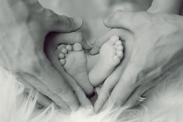 Schwarz-Weiss-Foto mit zwei Paar Händen, die um Babyfüsse ein Herz bilden