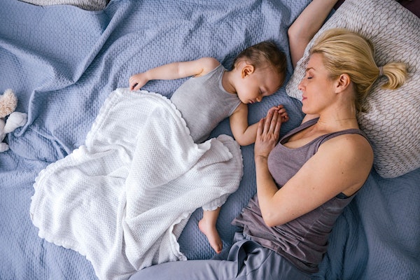 Kleinkind und Mutter am Schlafen in Bett, Tochter hält Mutters Hand