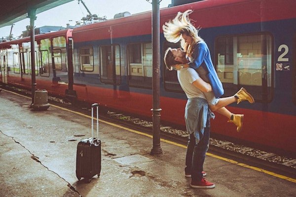 Am Bahnhof hält ein Mann die aufspringende Frau in seinen Armen. Ein Koffer steht daneben, ein Zug im Hintergrund.