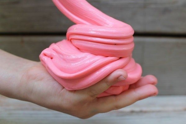 Eine Hand hält rosa Fluffy Slime mit Rasierschaum.