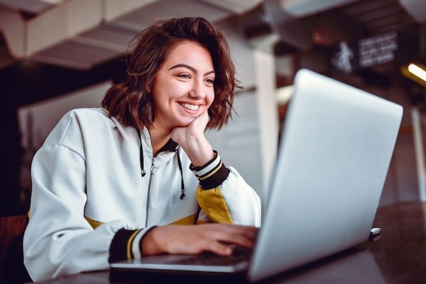 Eine junge Frau sitzt vor dem Laptop und lächelt.