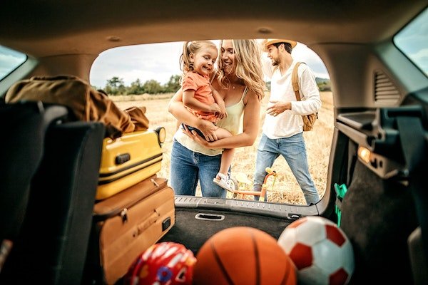 Kleine Familie steht hinter dem Kofferraum ihres Autos und ist bereit, in den Urlaub zu fahren.