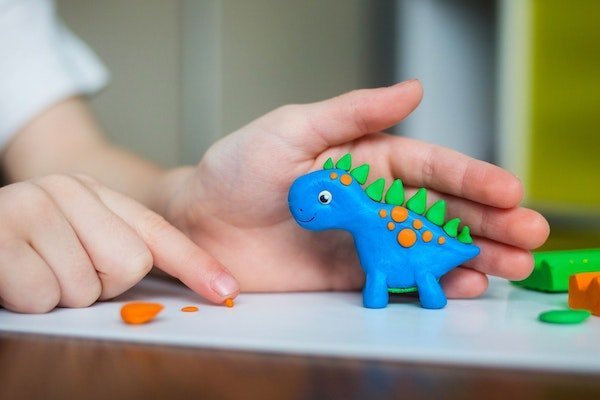 Ein Kind formt aus Knete einen farbigen Dinosaurier.