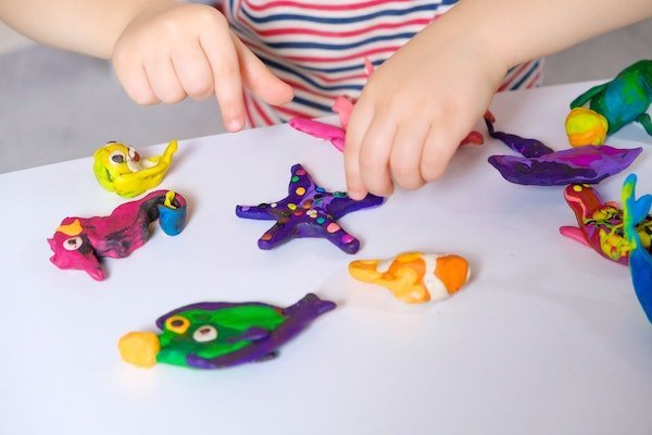 Kinderhände formen Knete auf einem weissen Tisch zu Unterwasserfiguren.