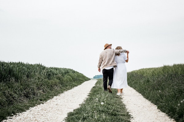 Ein Mann und eine Frau laufen auf einem Feldweg entlang. Er hält seinen Arm über sie.