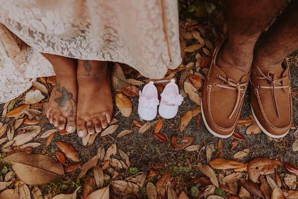 Ein Paar steht auf dem Boden. Zwischen ihren Füssen sind rosa Baby-Schuhe, die eine Schwangerschaft ankünden.