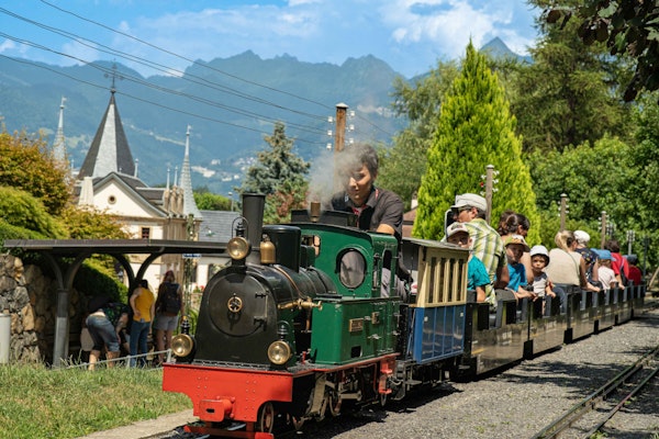 Eine kleine Dampflokomotive fährt durch den Park. Auf dem Zug sitzen viele Kinder.