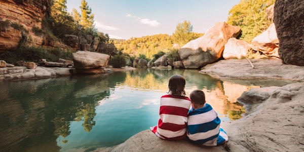 Deux enfants assis au bord d'une rivière dans les montagnes, enveloppés dans une serviette de bain