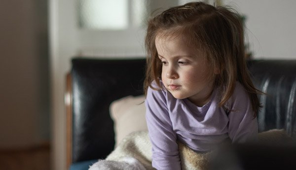 Long Covid Kinder: Petite fille assise dans son lit, fatiguée et sans énergie. 