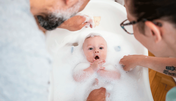 Baby baden: Vater und Mutter baden ihr Kind in der Babybadewanne