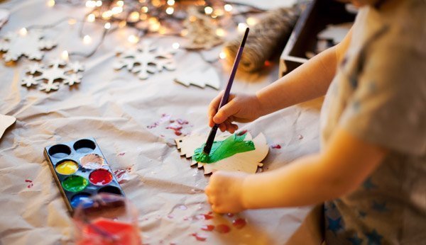 Kleines Kind bemalt mit Pinsel Tannenbäume und Sterne aus Karton als Christbaumschmuck
