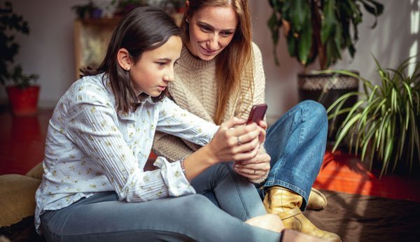 Belästigung im Netz: Teenager und Mutter schauen aufs Handy.