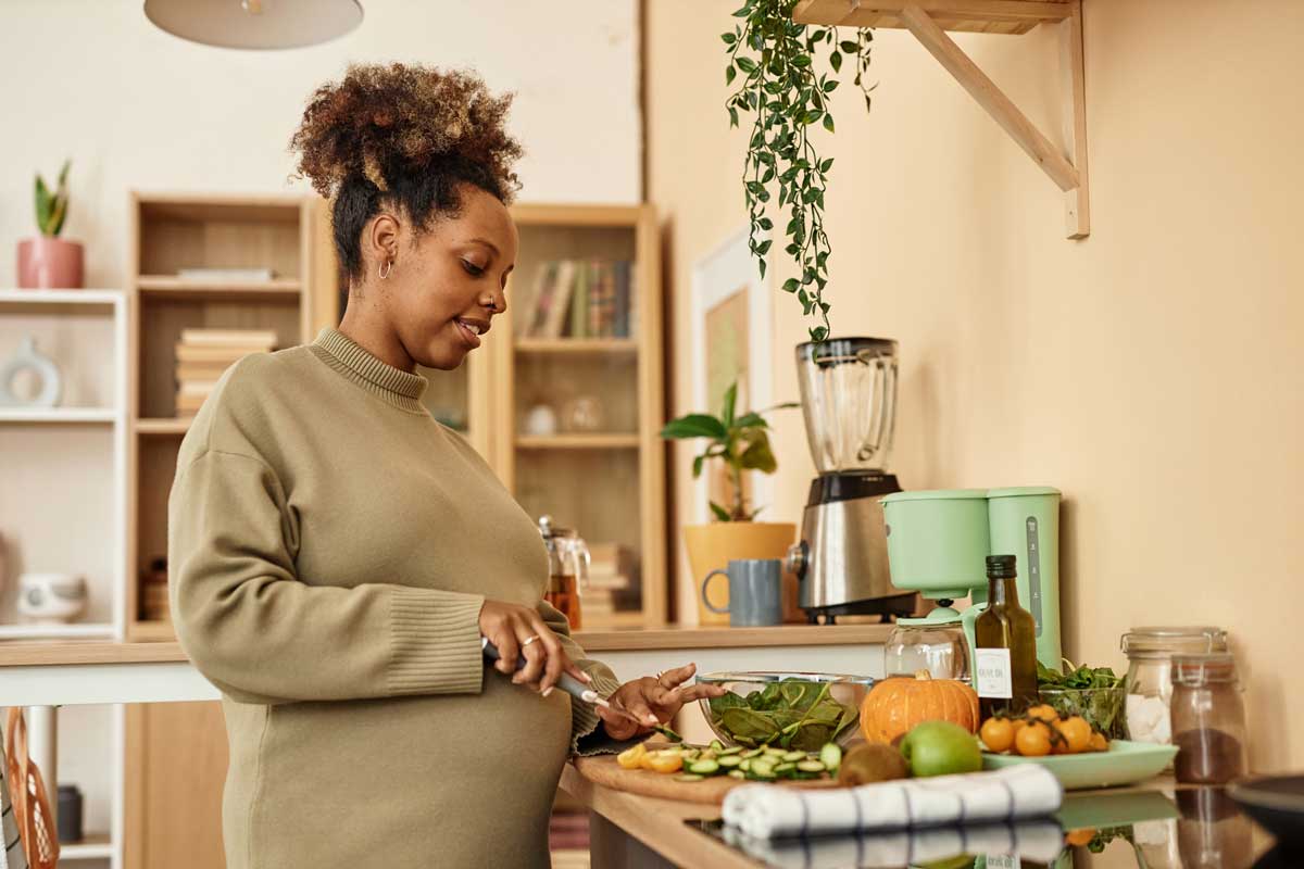 Eine schwangere Frau kocht mit viel Gemüse selber, um ihr Immunsystem zu stärken.