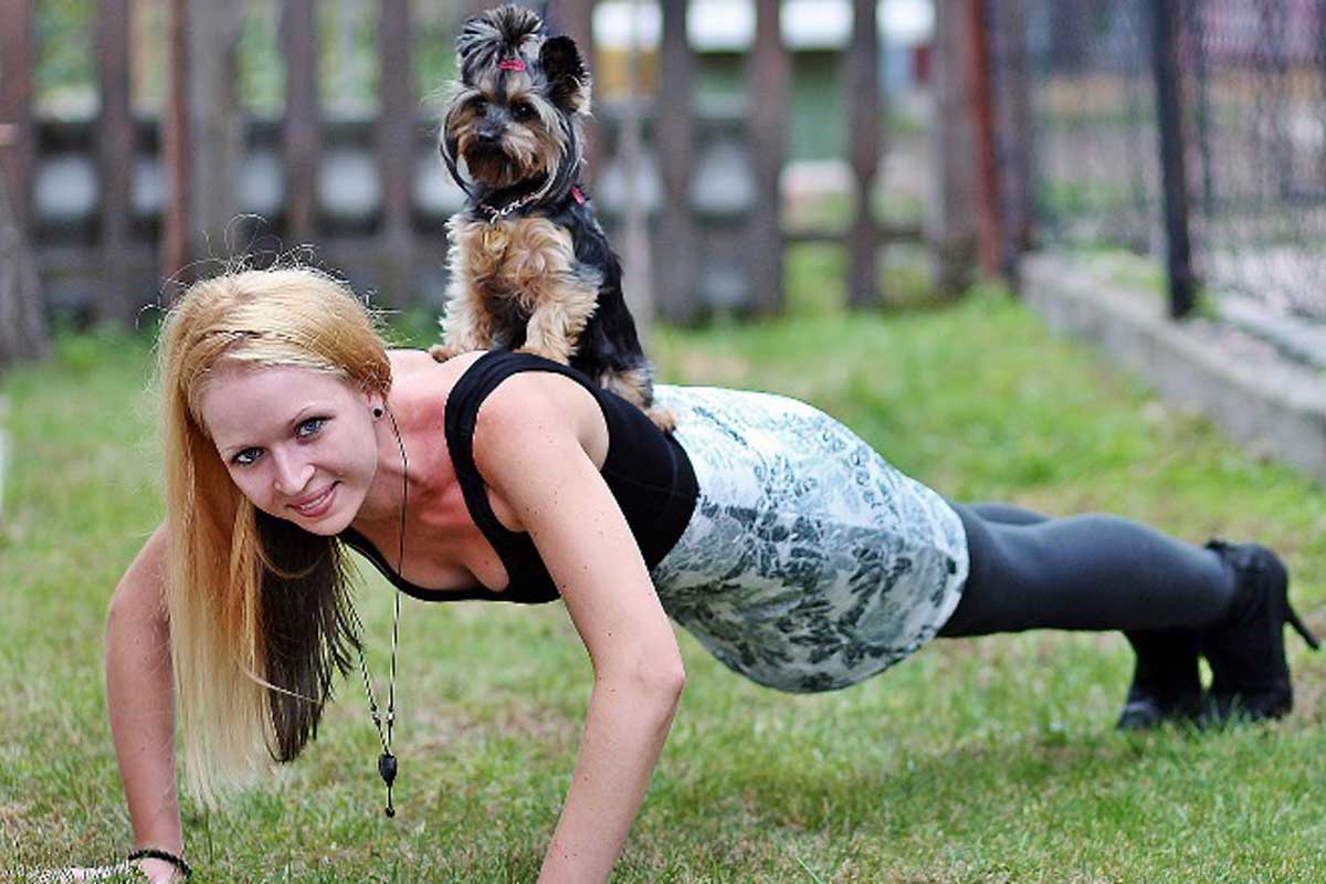Eine Frau macht im Park Liegestützen mit dem Hund auf dem Rücken.
