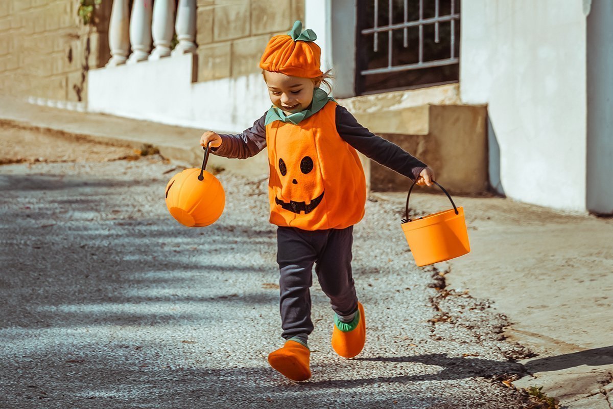 Fröhlicher kleiner Junge, der für Halloween als Kürbis verkleidet ist.