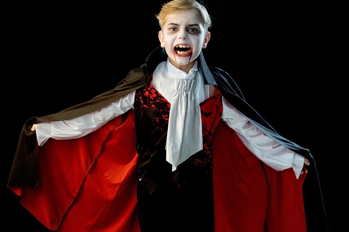 Ein Junge im Halloween-Vampir-Make-up und Kostümmantel, der seine Zähne entblösst.