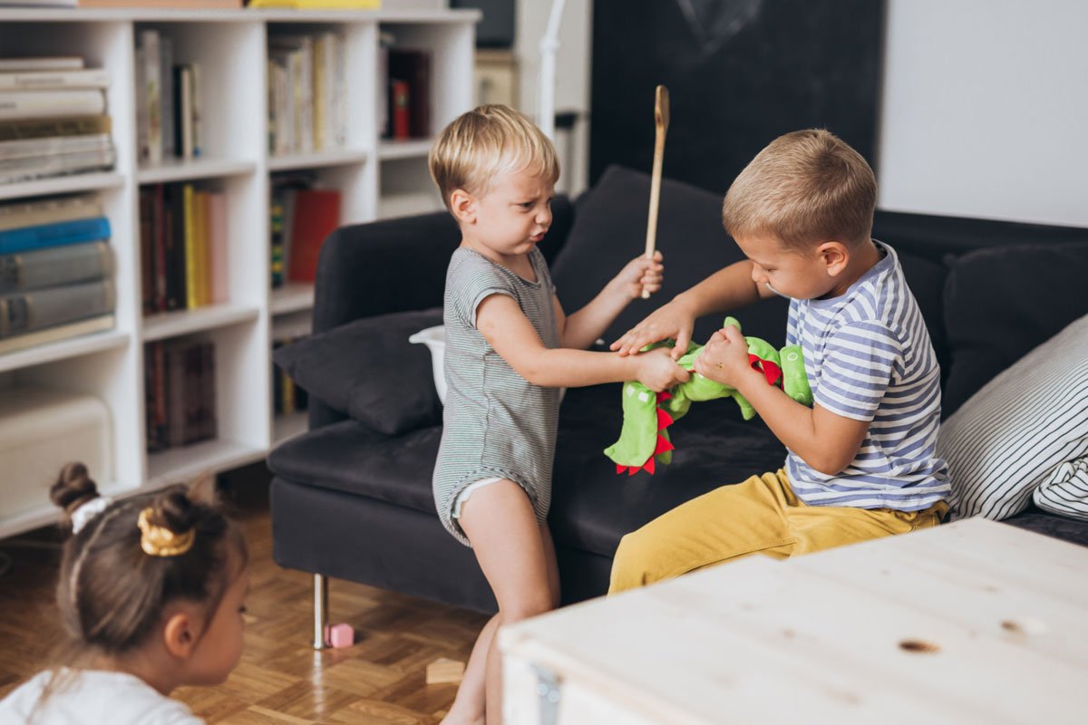Zwei kleine Jungen streiten um ein Spielzeug, der eine hält einen Kochlöffel und schlägt damit