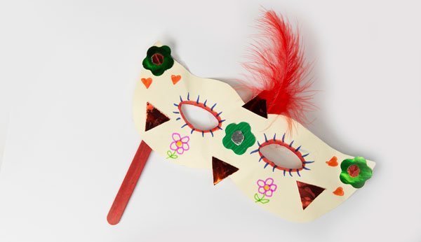 Karnevalsmaske selbstgemacht und bemalt an einem Holstengel vor weissem Hintergrund