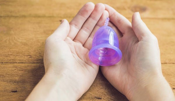 Coupe menstruelle: Une femme tient une coupe menstruelle violette dans ses mains.