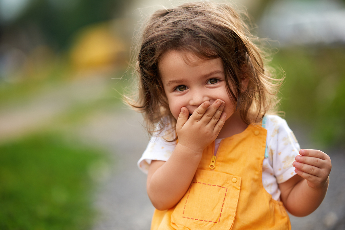 Ein Mädchen lacht verlegen und hält sich die Hand vor den Mund.