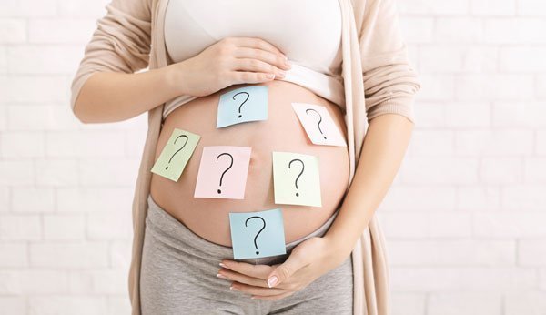 Procura de nomes: Uma mulher grávida cola notas com pontos de interrogação no estômago.